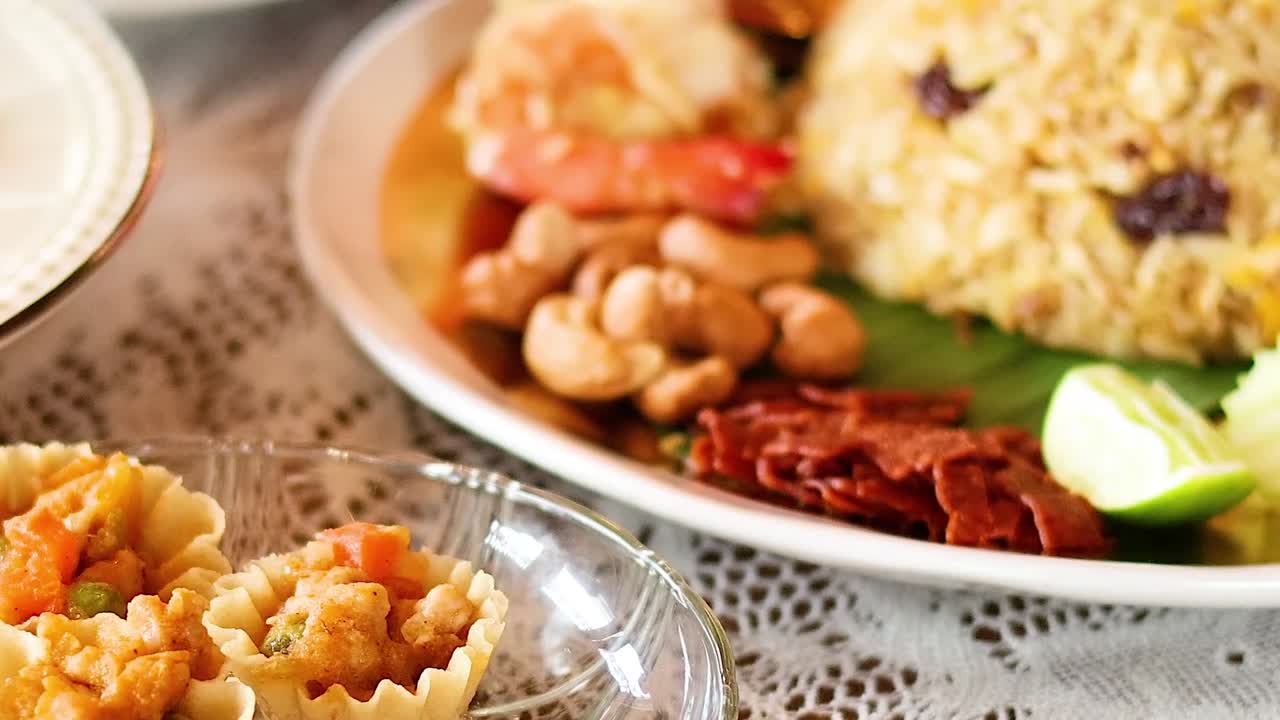 Close-up of a hand selecting Thai tartlets from a decorative plate on a lace tablecloth.