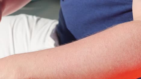 close-up of a person applying lotion to their arm under bright sunlight, focusing on skin care.