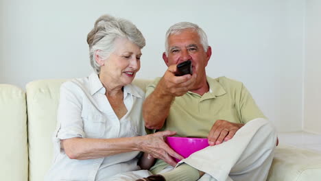 Senior-couple-sitting-on-sofa-watching-tv