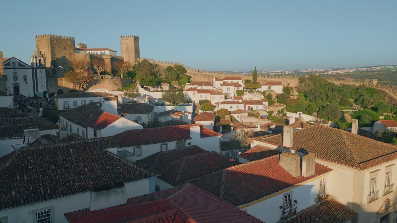 Red tiled town rooftops under soft evening light drone view. Stone castle walls