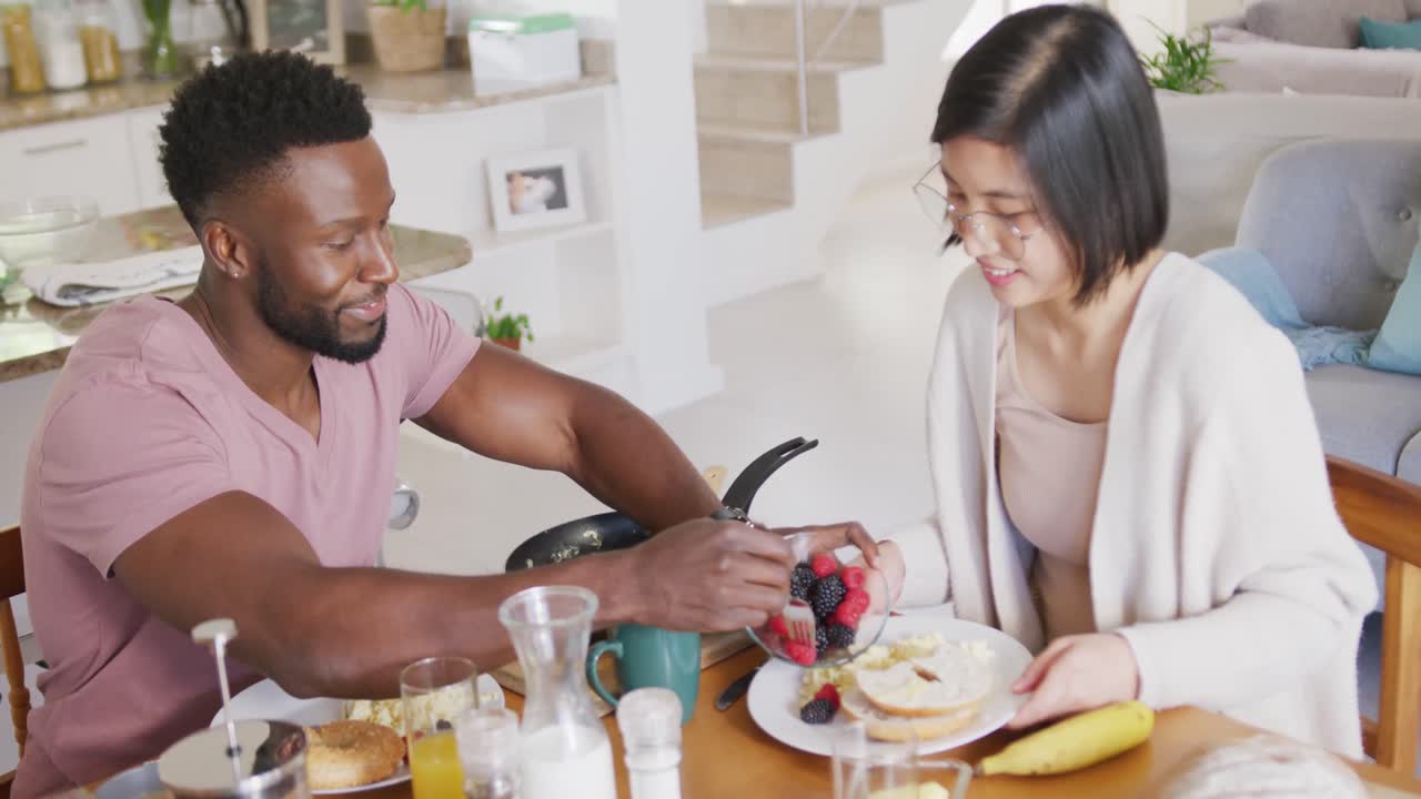 Happy diverse couple sitting at table and having breakfast