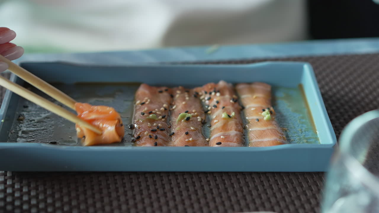 Una donna con le bacchette in mano prende sottili fette di salmone marinato con sesamo, erbe aromatiche e salsa