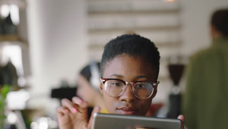 portrait beautiful african american woman using digital tablet computer in cafe browsing online reading social media messages watching entertainment wearing glasses