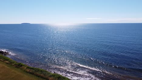 aerial drone flying over grass cliff revealing the ocean with clear blue sunny sky in the maritimes, canada