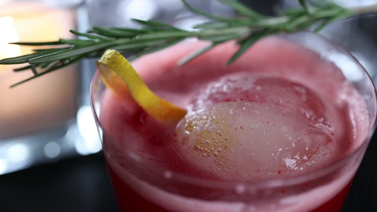 primer plano de un cóctel rojo con romero y limón