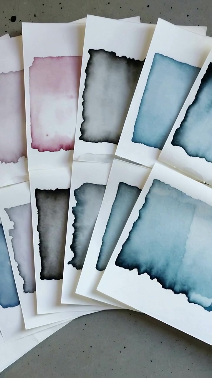 Vertical video: Panning top cam at start over watercolor sheets on gray table showing blue wash