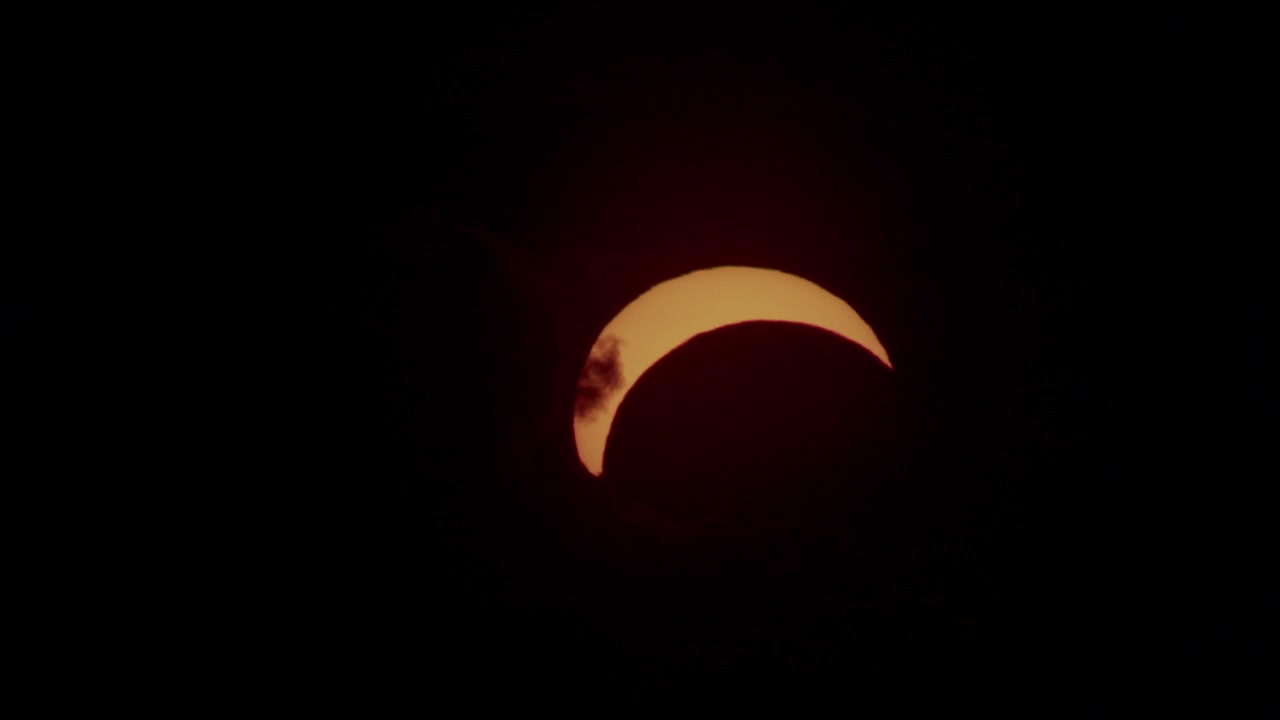 Partial solar eclipse through clouds in sunset moment near horizon