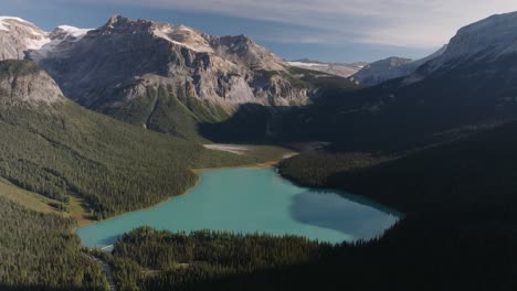 aerial dolly out of emerald lake louise surrounded by dense pine tree forest and mountains at banff national park, alberta, canada