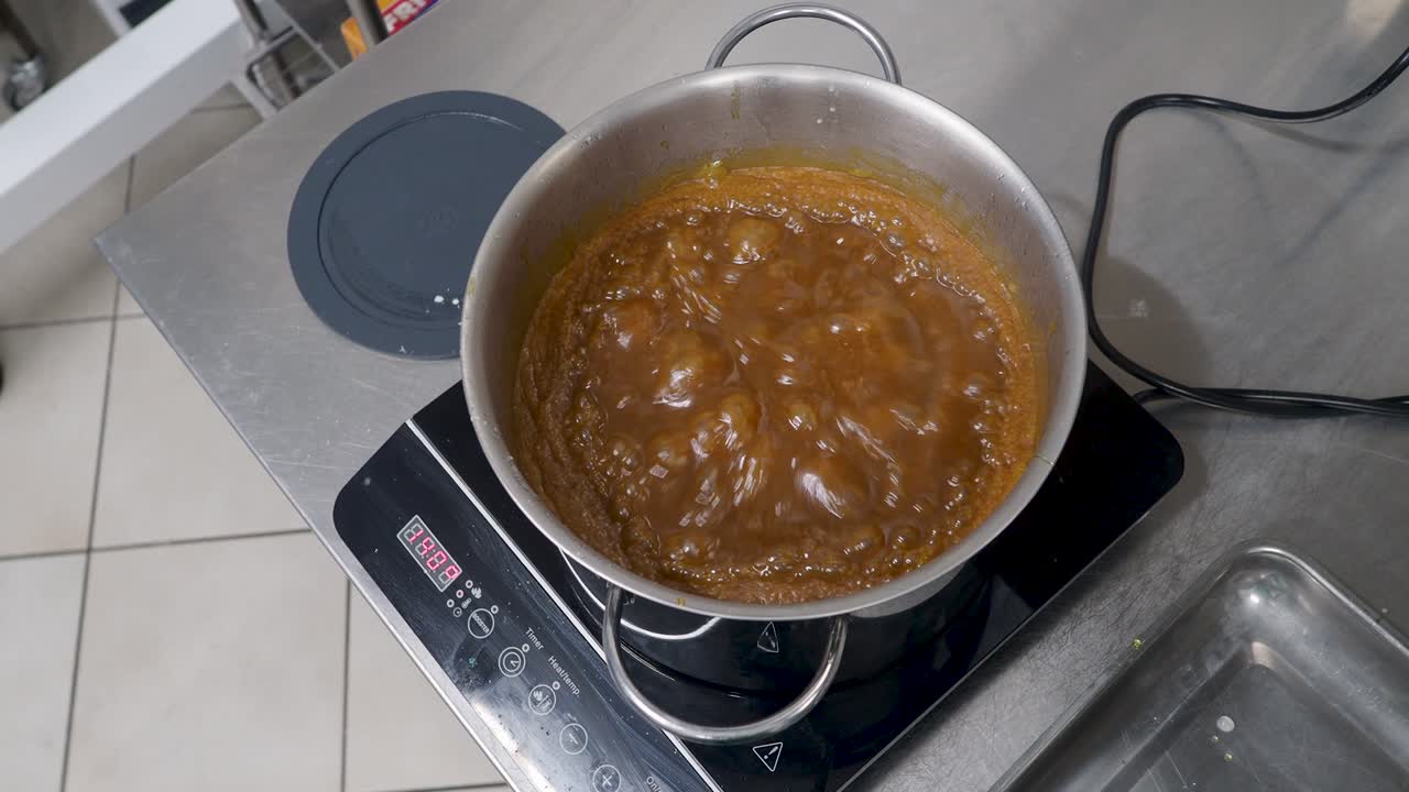 chef cooking salted butter caramel dessert , boiling, styr with spatula, hot smooth cooked salty sauce in steel pan on stove