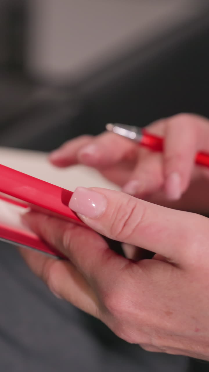 Nærbillede af person, der holder en rød telefon i den ene hånd og skriver med en rød pen i en notesbog, hvilket viser fokus på den aktuelle opgave. Ideel til forretningsmøder, kontorarbejde og produktive sessioner.