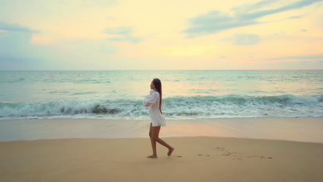 a lovely young woman walks along a sandy beach leaves footprints that are soon washed away by the incoming waves