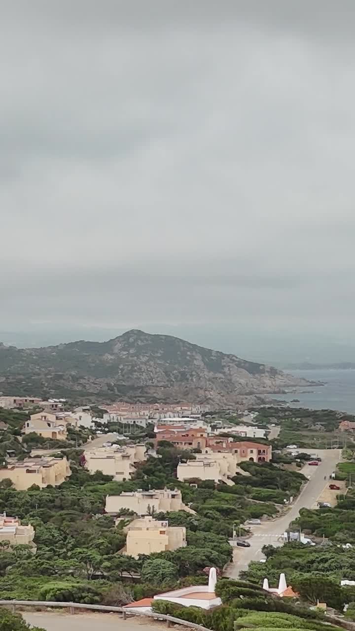 Vista della costa della Sardegna con case e rocce sotto un cielo nuvoloso al mattino presto