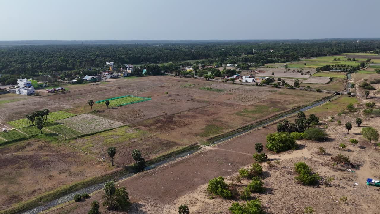 Aerial view of a small, colorful Hindu temple complex in rural South India. Features include traditional temple buildings and a prominent statue of a deity on a sandy ground