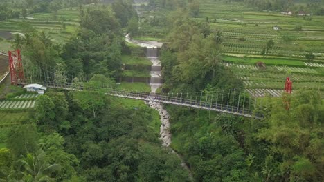 Vista-Aérea-De-Drones-Del-Puente-Colgante,-Valle-Y-Río-Con-Cascadas