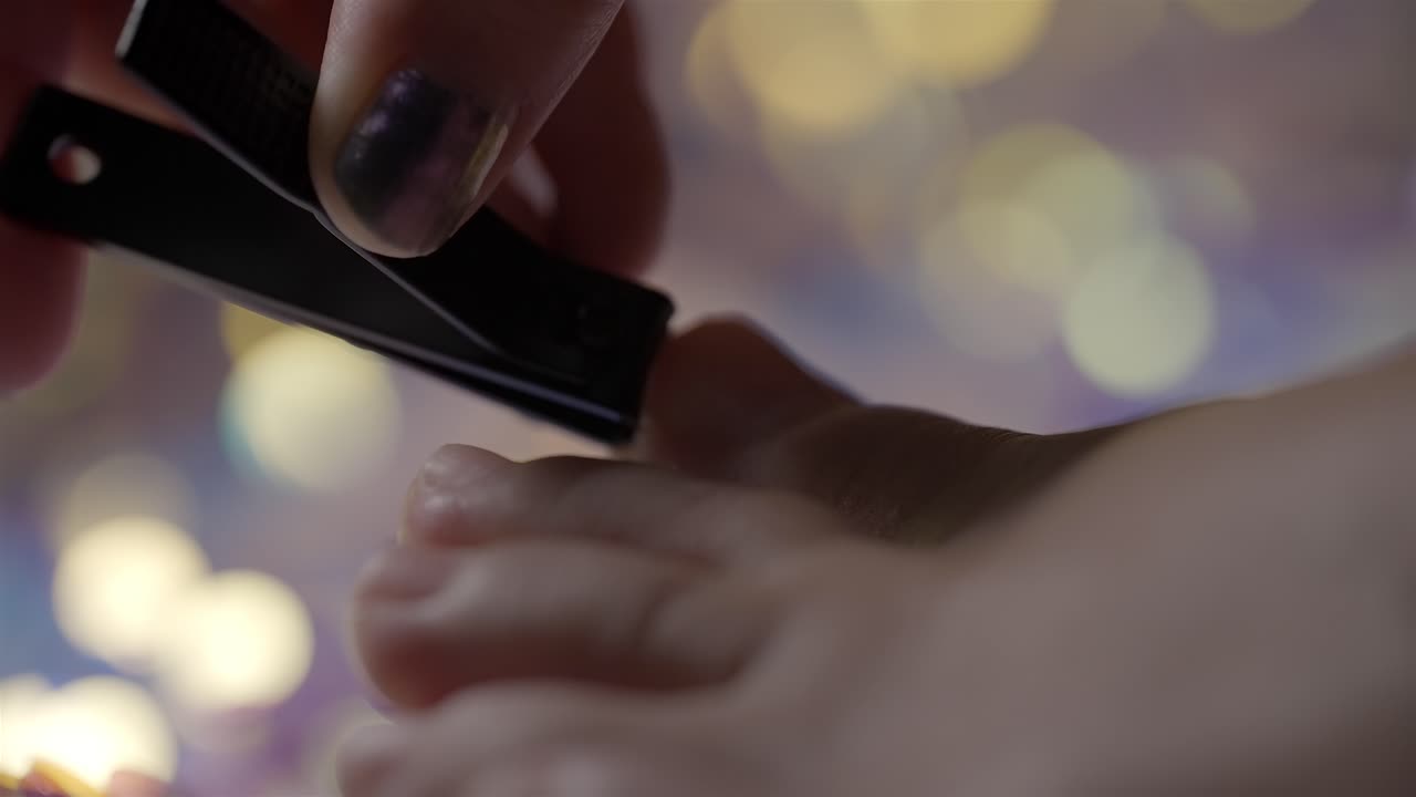 Slow-motion close-up shows a woman trimming toenails with a clipper against a bokeh backdrop