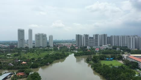 Steigender-Drohnenschuss,-Der-über-Den-Fluss-Fliegt,-Mit-Hochmodernen-Wohnhochhausentwicklungen-Mit-Interessanter-Architektur-Und-Dramatischem-Himmel