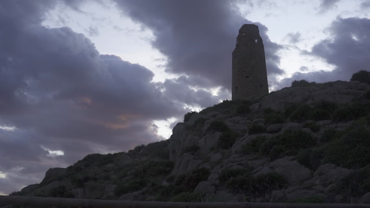 hermosas vistas de una torre centenaria en la cima de una montaña, el cielo nublado dibuja colores naranjas sobre las nubes al atardecer