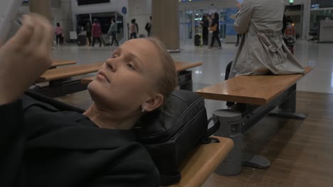 Woman-waiting-in-airport-lying-on-the-bench-with-pad