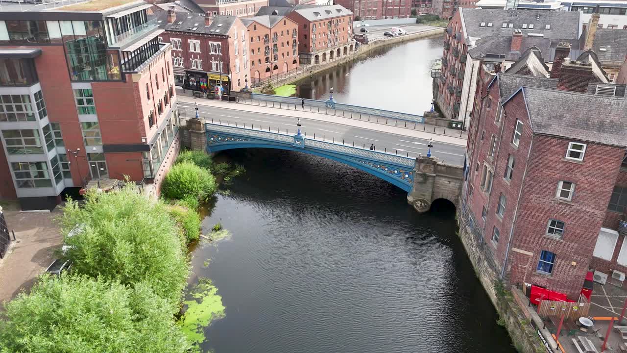 Aerial camera smoothly pans across a Victorian bridge, river, and historic cityscape in Leeds, England, under bright daylight with soft shadows