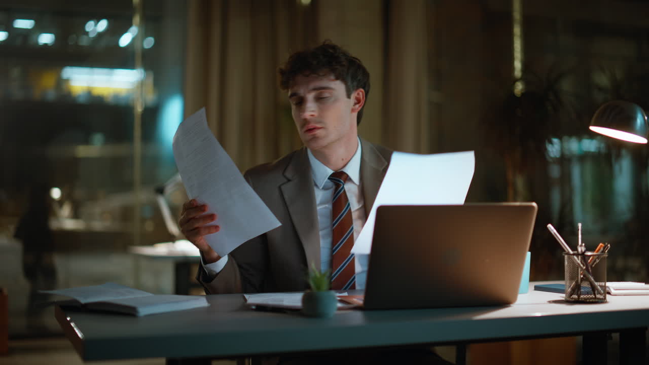Focused manager doing paperwork at night office closeup. Smiling man rejoicing