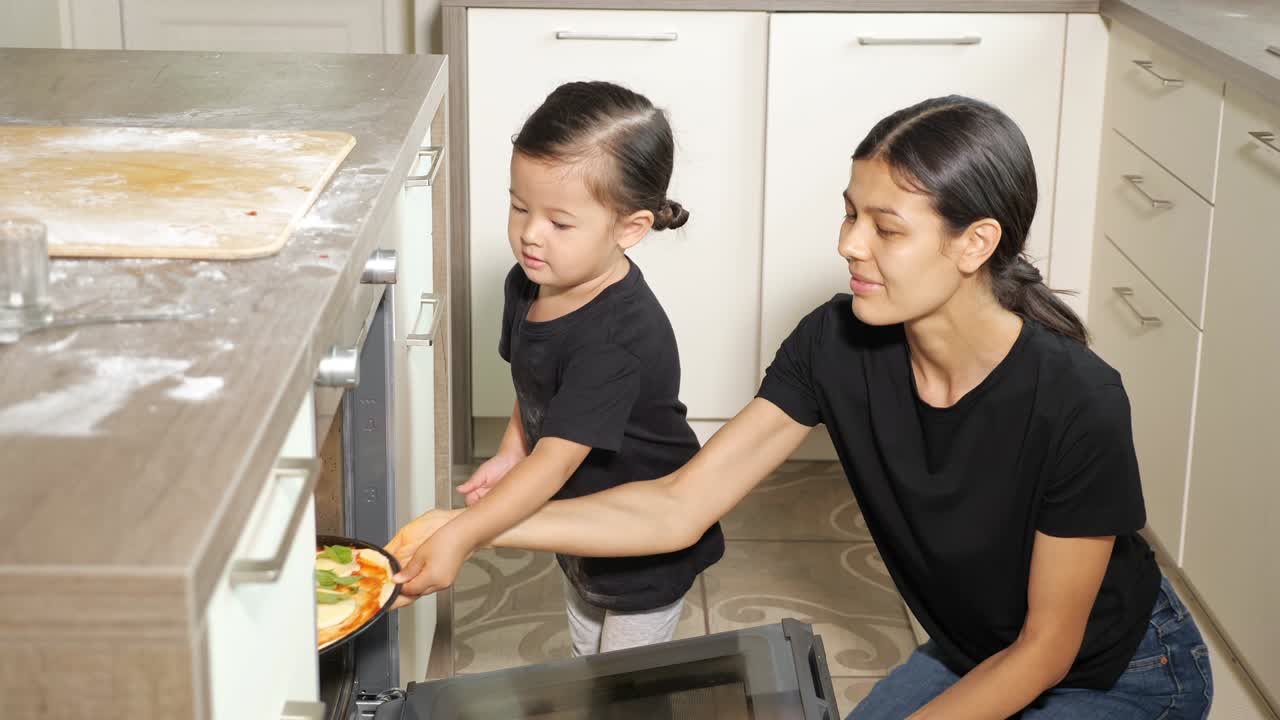 la niña ayuda a su madre a poner una deliciosa pizza en un horno moderno.