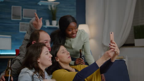 multiracial friends resting on sofa enjoy spending time together while taking selfie