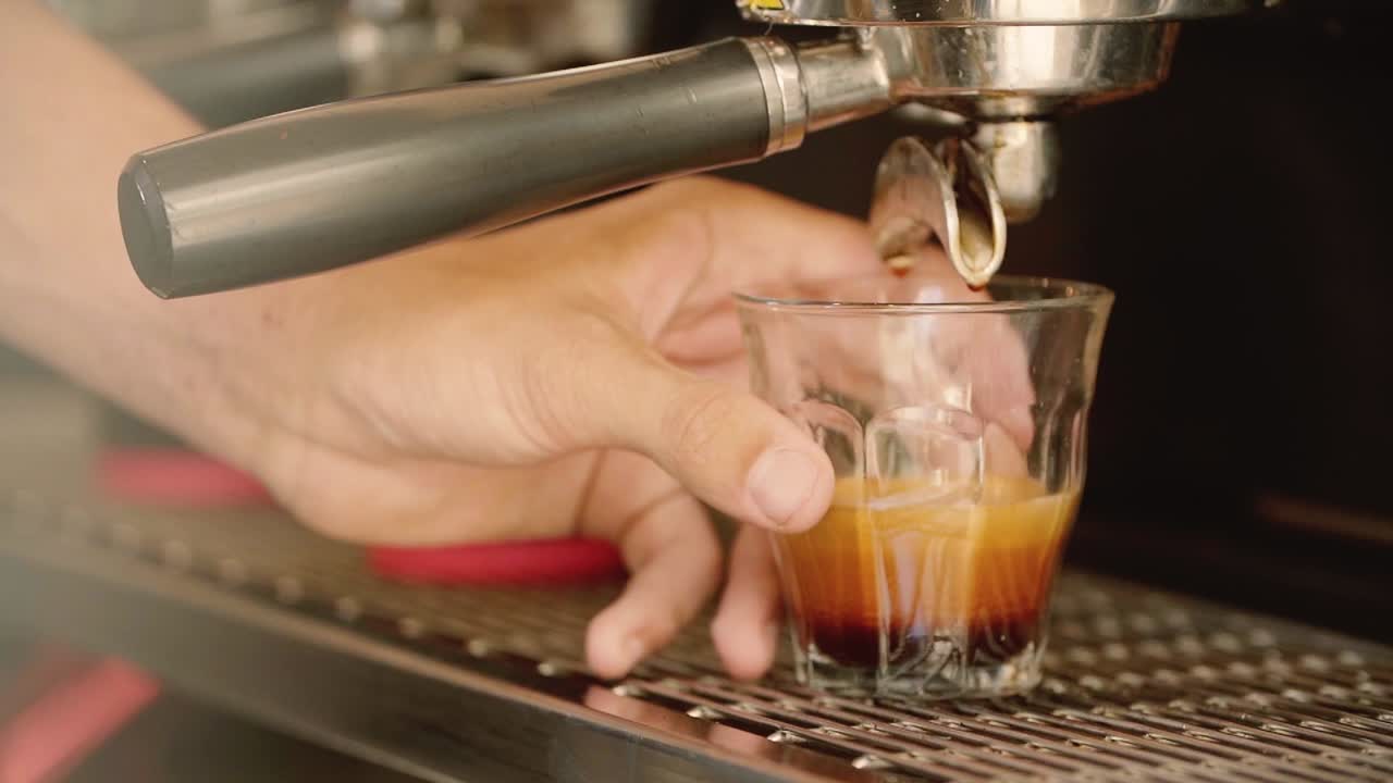 Slow-motion close-up of a barista’s hand picking up a glass of espresso from a coffee machine