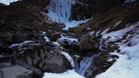 Hielo-En-El-Acantilado-Con-Cascada-Grundarfoss-Que-Desemboca-En-El-Río-Rocoso-En-Invierno-En-Islandia