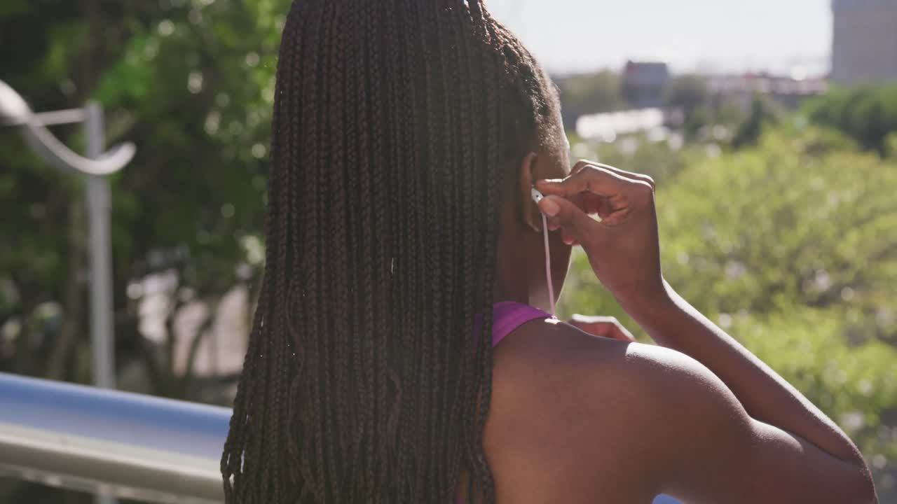 African american woman wearing earphones while standing on the city bridge