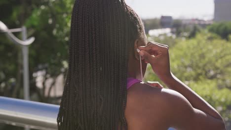 african american woman wearing earphones while standing on the city bridge