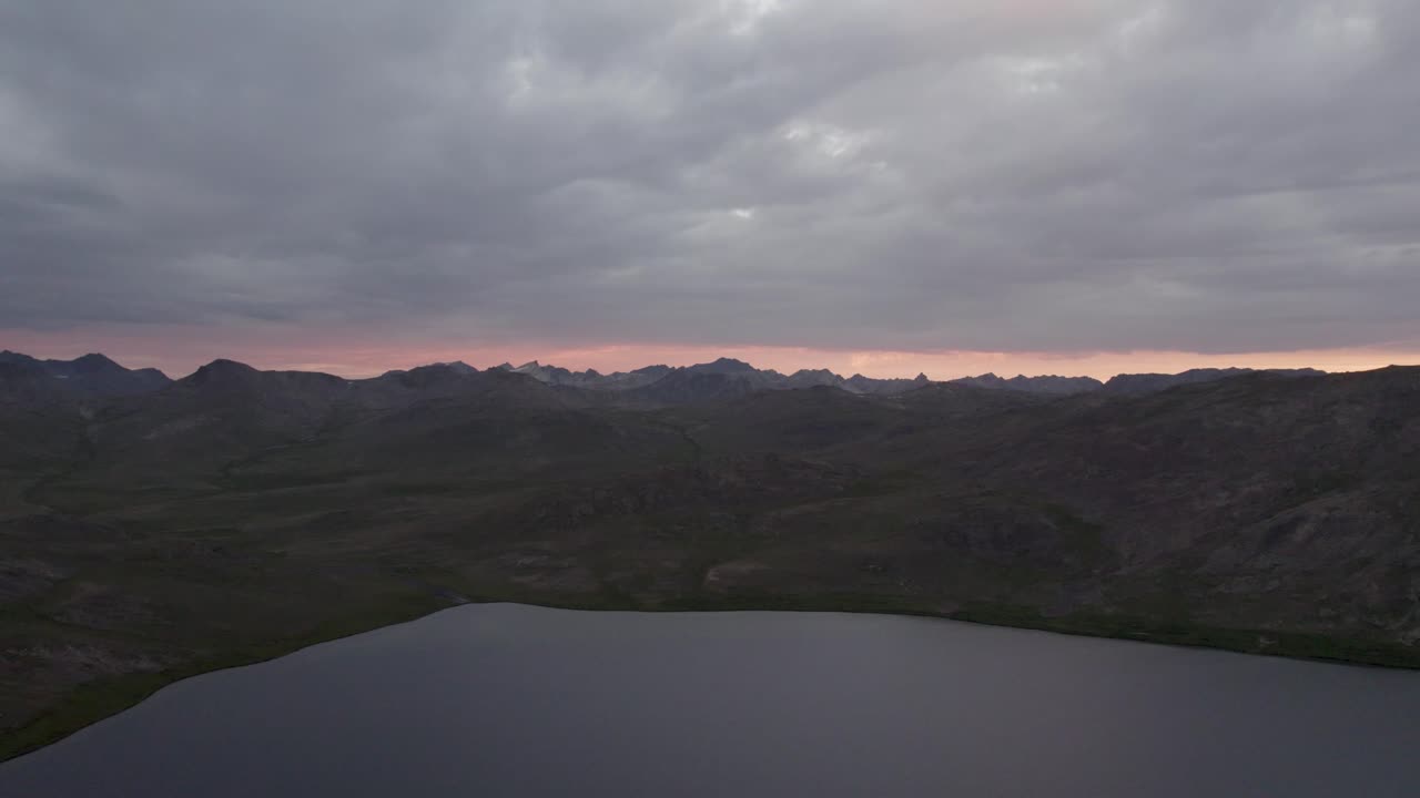 Twilight view of Sheosar Lake with dark hills and distant peaks under dramatic cloudy skies. Deosai, Pakistan