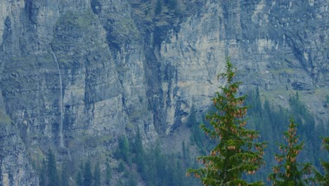 a waterfall runs out from the middle of an imposing cliff