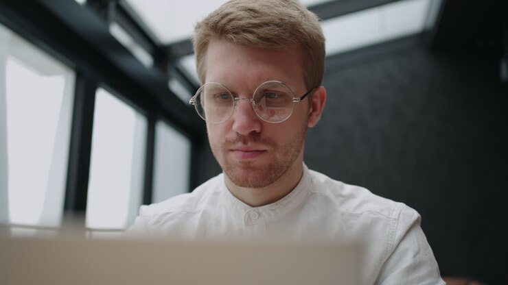 ein stilvoller mann mit brille arbeitet mit einem laptop konzentriert und mit einem ernsten gesicht