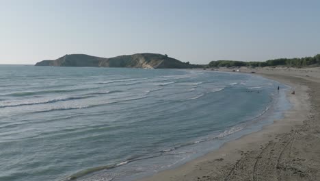 Zeitlupenwellen,-Die-Sich-Entlang-Eines-Leeren-Strandes-Mit-Bäumen-Und-Klippen-Bewegen