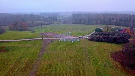 Aerial-towards-flight-to-worker-installing-new-transmission-tower-in-rural-area-during-cloudy-day