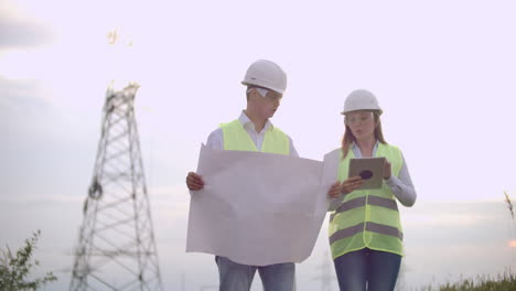 un grupo de ingenieros en una central eléctrica de alto voltaje con una tableta y dibujos caminan y discuten un plan para el suministro de electricidad a la ciudad.