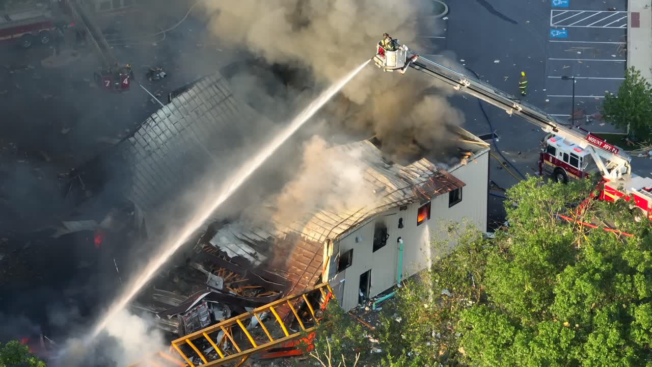Vigile del fuoco su scala che spruzza acqua su un edificio in fiamme dopo un'esplosione in una città americana - Ripresa aerea dall'alto