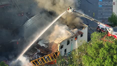 firefighter on ladder spraying with water on burning building after explosion in american city - aerial top down