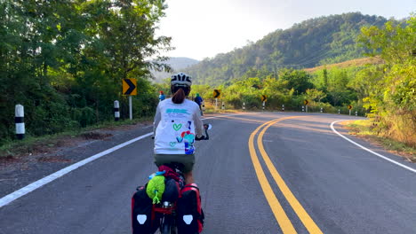 back view of women cycling in the forest road of nan province, thailand