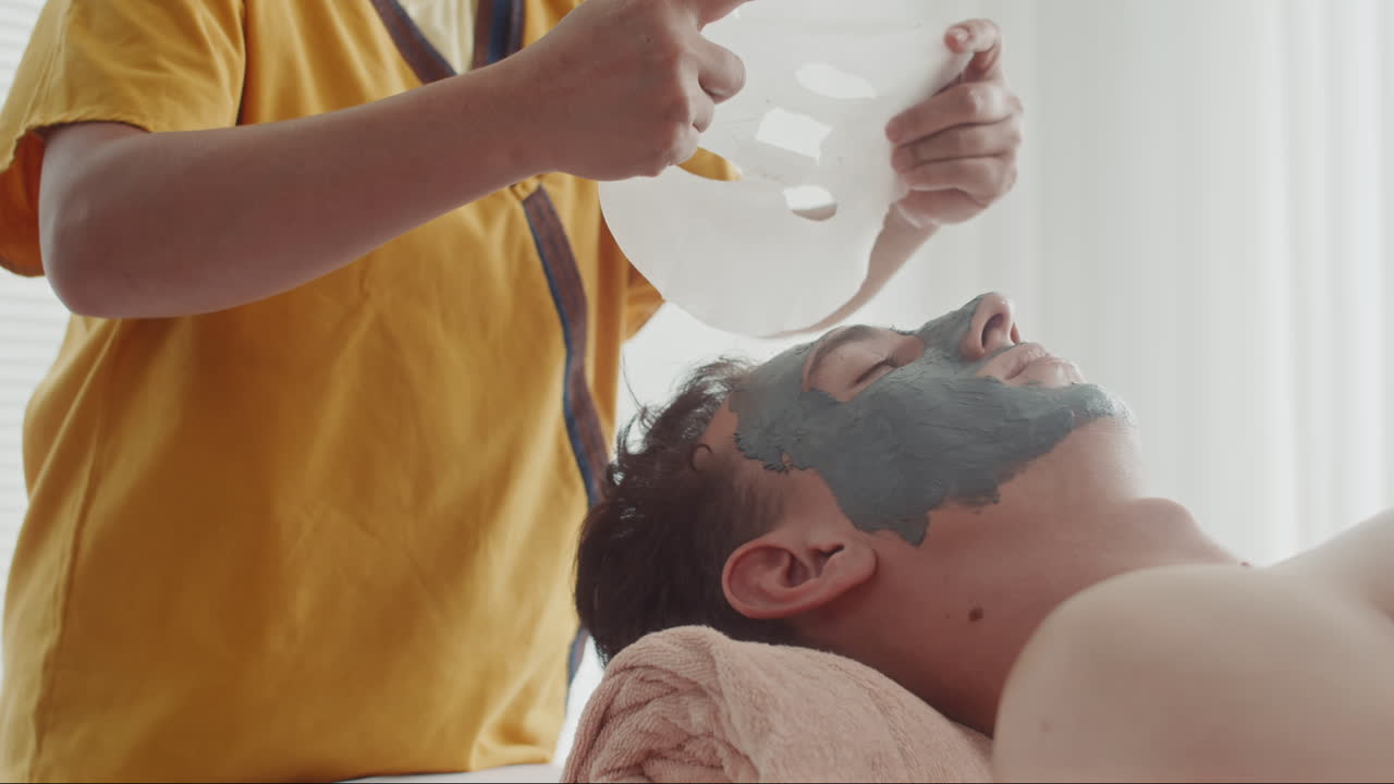 Cosmetologist Putting Sheet Mask on Face of Man