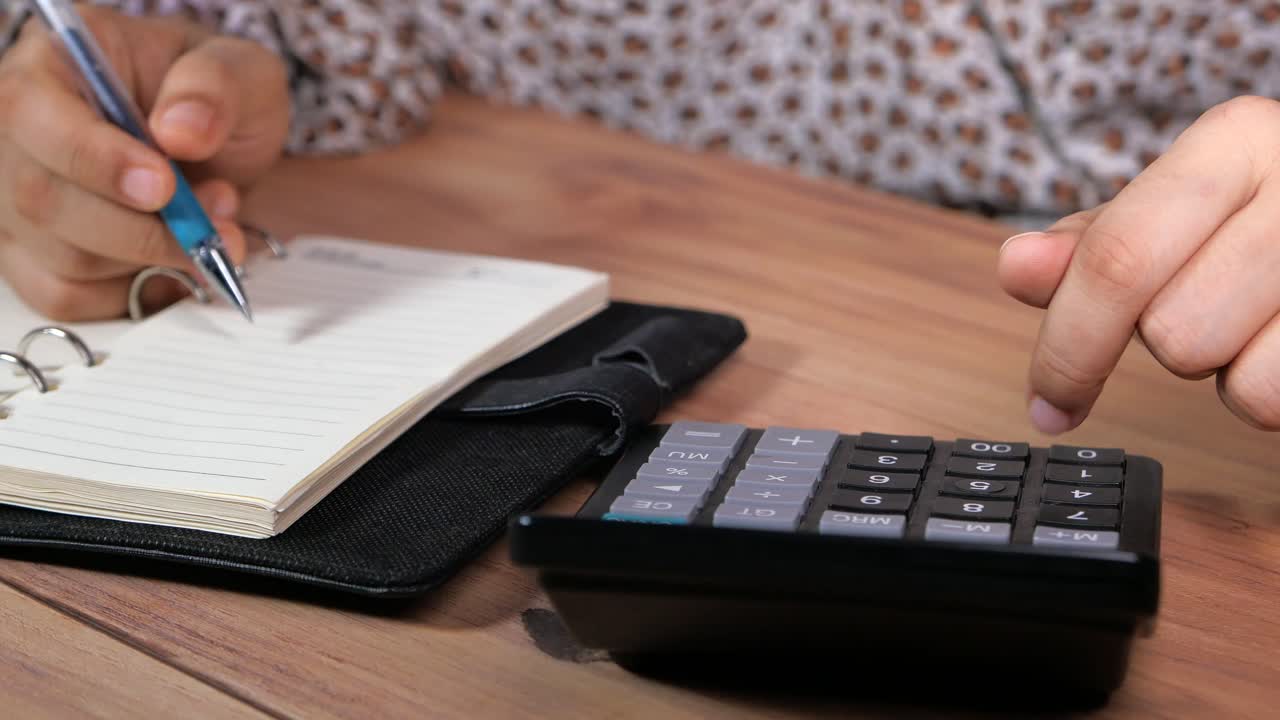 persona que hace cálculos en un bloc de notas y una calculadora