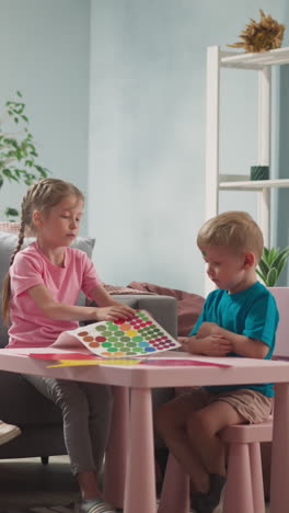 woman works at laptop at home, children next to their mother glue stickers at table, developing activities