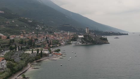 Drone-shot-of-Malcesine-town-with-the-castle-on-a-rock-on-Lake-Garda-and-mountains-around-it