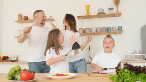 american parents and children have fun in the kitchen they dance while holding kitchen utensils american parents and children have fun in the kitchen they dance while holding kitchen utensils joyful young family