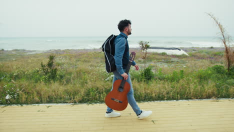 man walking with his guitar in hand on the sidewalk near the sea