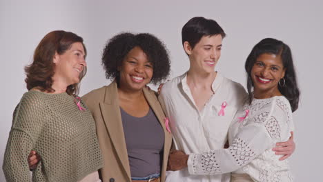 Studio-Portrait-Of-Multi-Racial-Group-Of-Smiling-Women-Of-Different-Ages-Wearing-Pink-Breast-Cancer-Awareness-Ribbons-Hugging-Against-White-Background