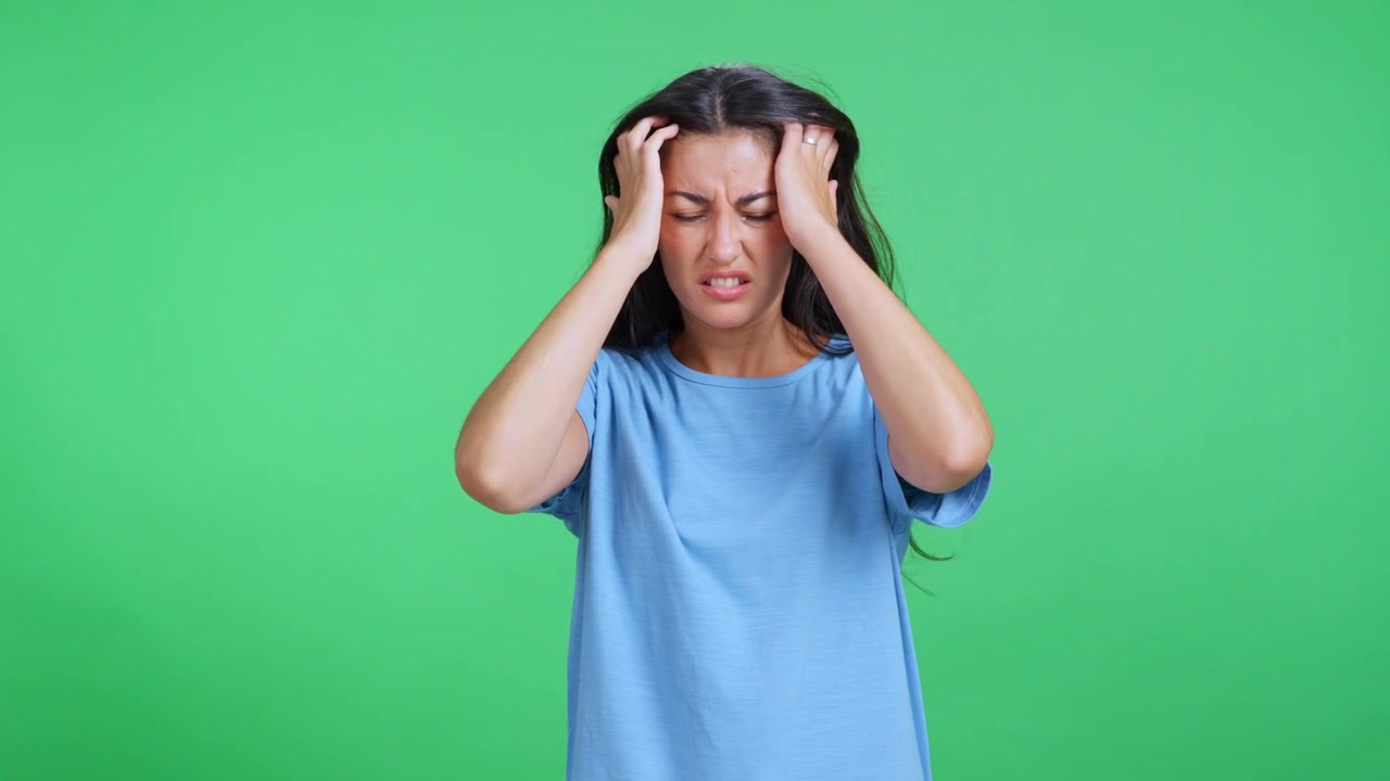 Young Woman Suffering From a Severe Headache Against a Green Screen