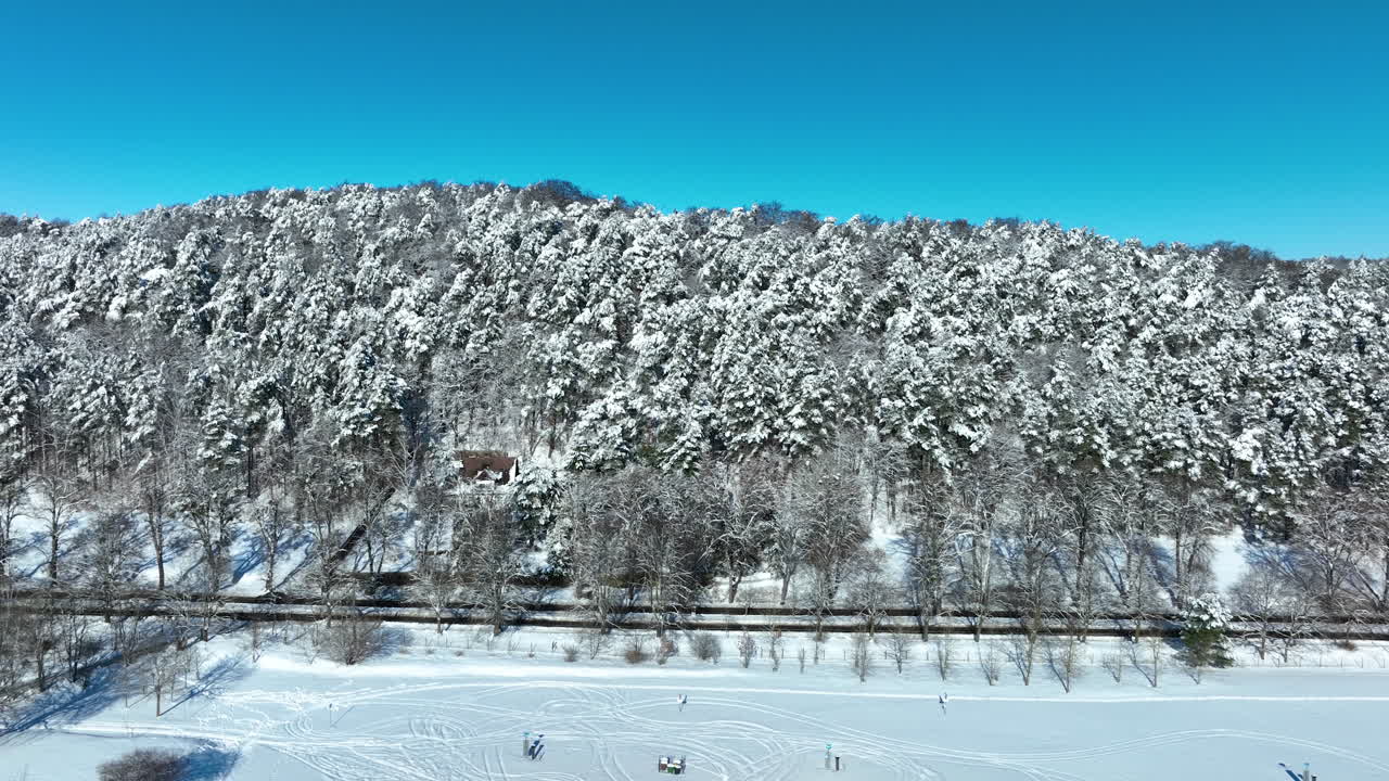 ポーランド、グダニスクの澄み切った青空の下、線路の隣に広がる、真っ白な新雪に覆われた鬱蒼とした松林の息をのむような空撮ショット。