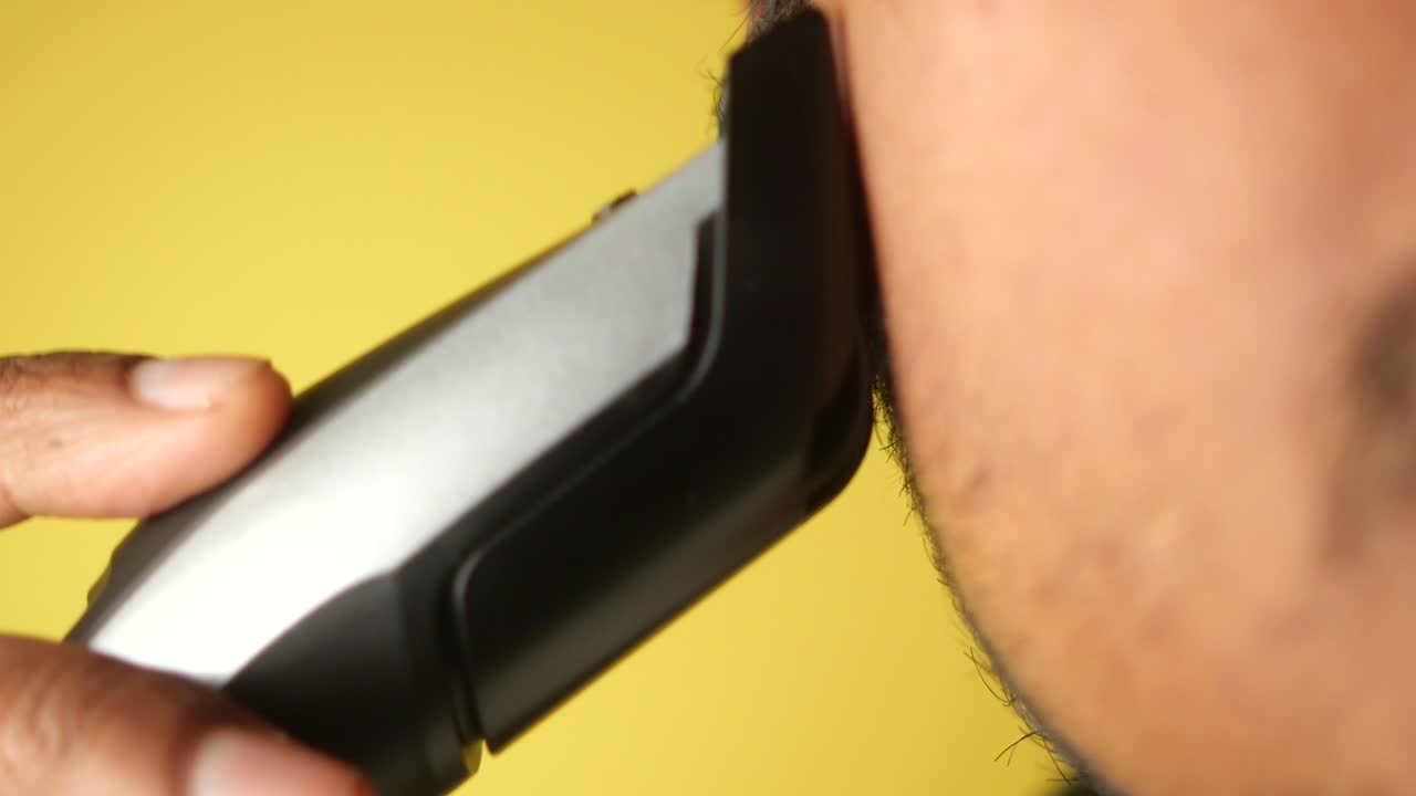 남자 가 전기 트리머 로 수염 을 면도 하고 있다