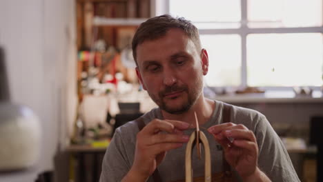 bearded worker makes seam on leather piece in craft workshop